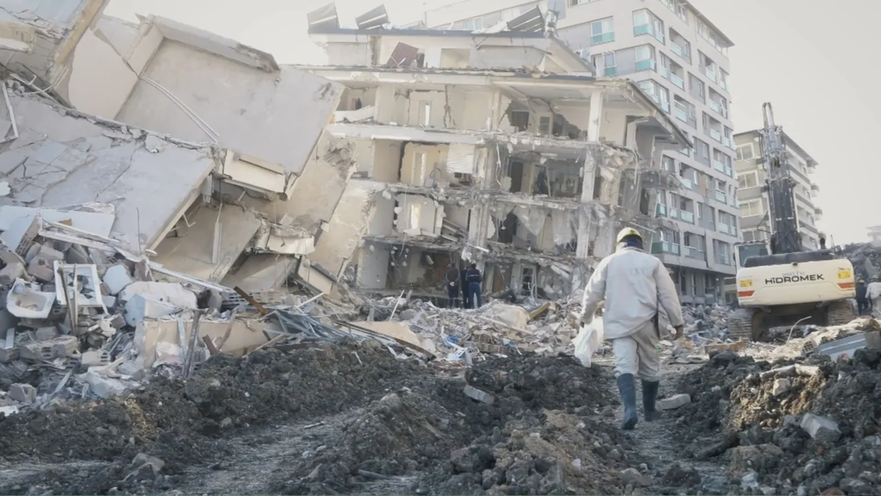 Death Without Mercy (2024) movie still: wide — A decimated multi-story concrete building sits in ruins amidst mounds of scattered industrial debris.…