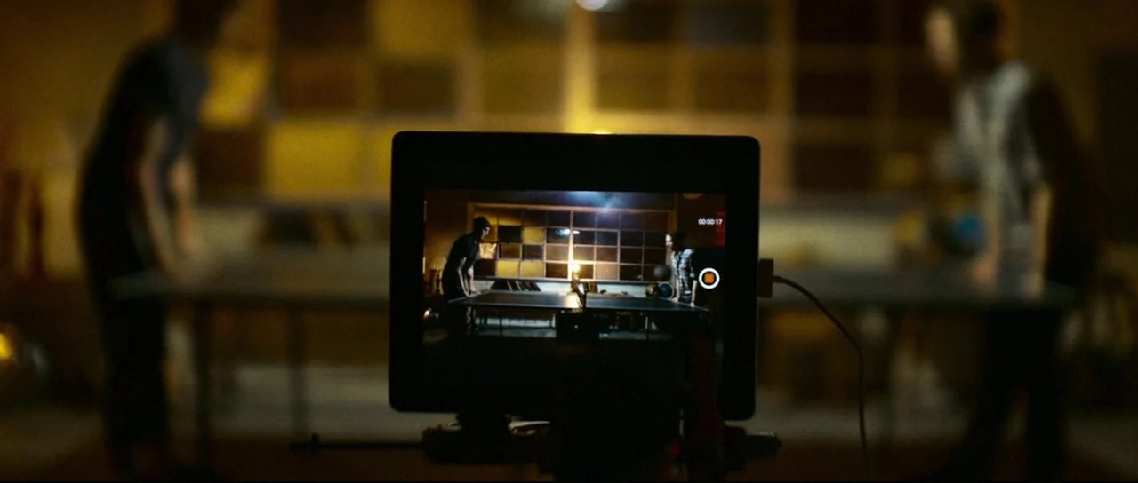 Depraved (2019) movie still: medium — A digital tablet screen sits in the center of the frame capturing two figures playing ping pong. Two blurred…