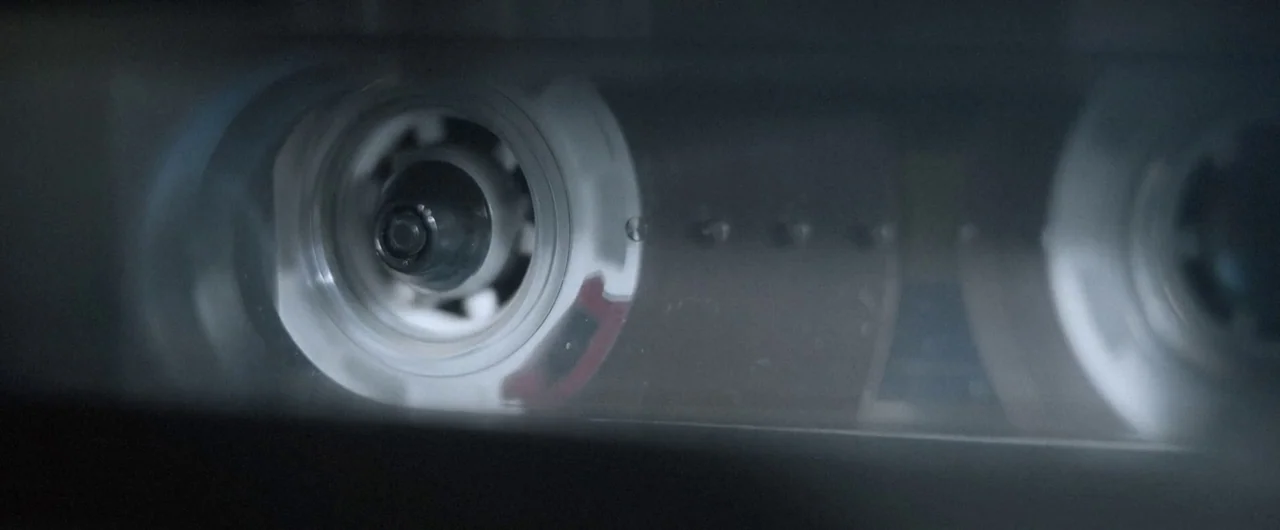 No Man of God (2021) movie still: closeup — A close-up view shows the internal mechanism of a cassette tape housing. Plastic spools and transparent…