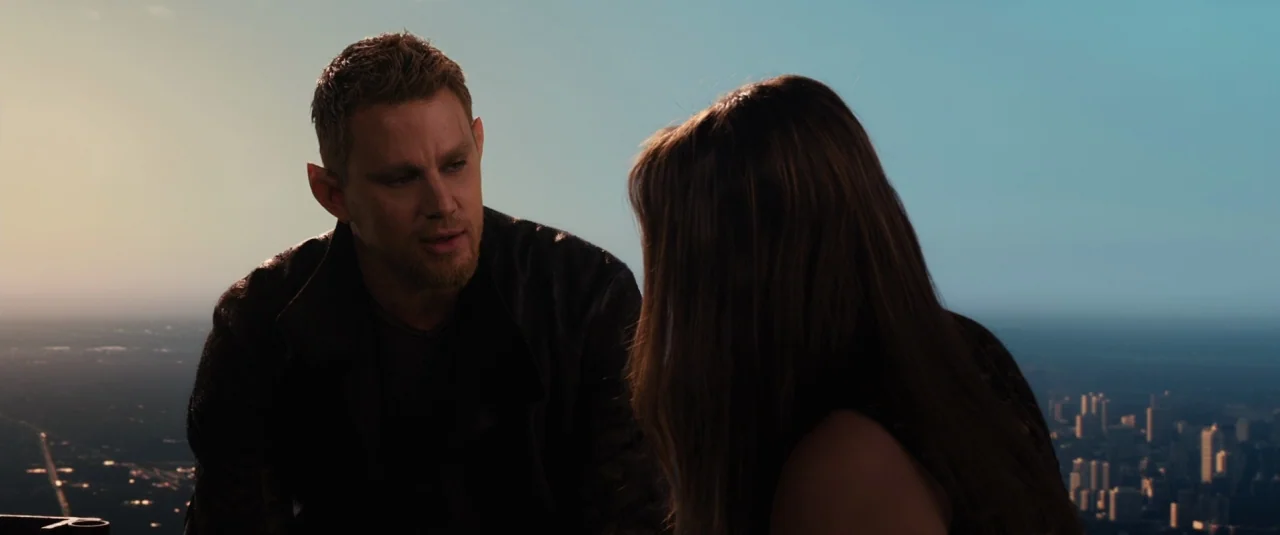 Jupiter Ascending (2015) movie still: medium — Two individuals sit atop a tall building overlooking a sprawling urban landscape at sunset. The man…