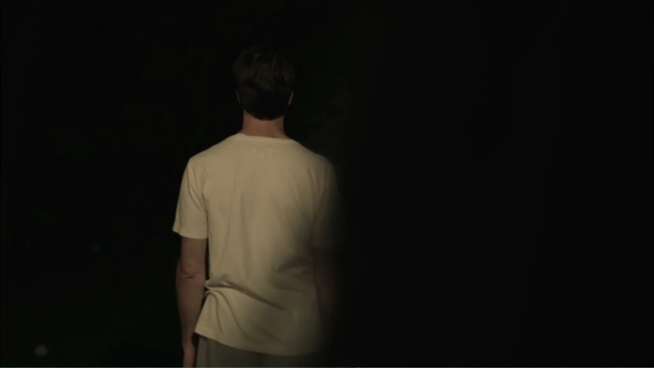 Dark Skies (2013) movie still: medium — A dark, undefined space with a subject positioned on the left side of frame. A lone man stands with his back…