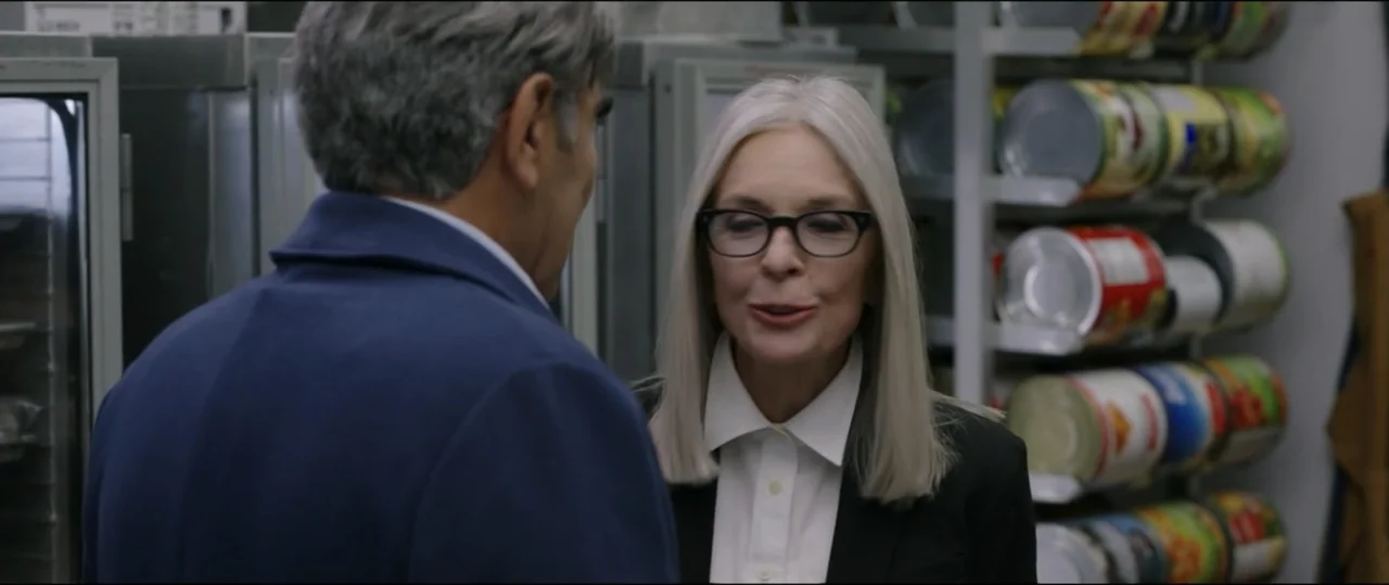 Summer Camp (2024) movie still: medium — A food pantry storage area features metal shelves stacked with numerous large tin cans. A woman addresses a…