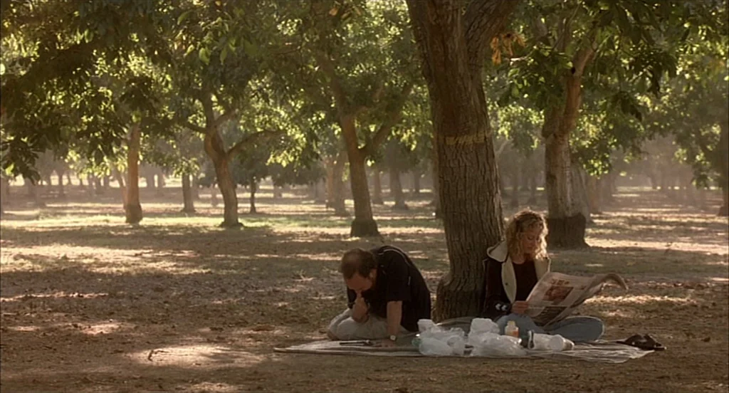 Sideways (2004) movie still: wide — Two people rest on a blanket in the middle of a dense orchard. A man crouches near a picnic spread while a woman…
