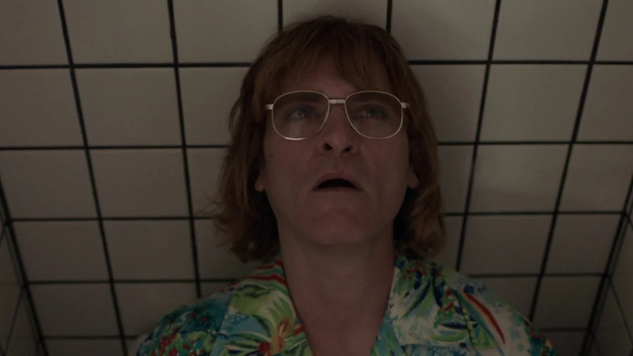 Don't Worry, He Won't Get Far on Foot (2018) movie still: closeup — A man stands against a wall covered in white square tiles with black grout. The…
