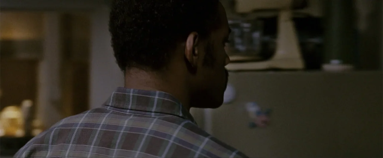 The Pursuit of Happyness (2006) movie still: closeup — A dark kitchen interior featuring an out-of-focus refrigerator and appliance in the…