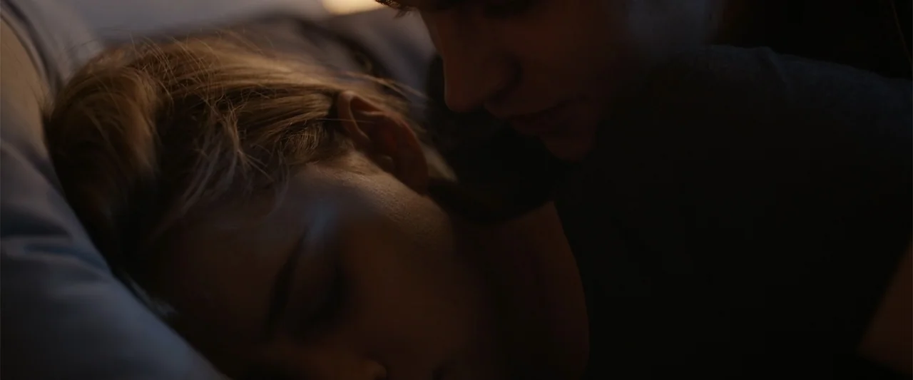 After Ever Happy (2022) movie still: closeup — A dark bedroom shows two people lying close together on a bed. The man leans slightly toward the…