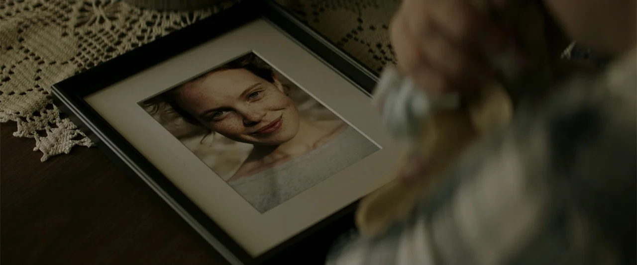 K.G.F: Chapter 2 (2022) movie still: closeup — A framed photograph lies on a wooden surface covered by a lace doily. A person's blurred hand rests…