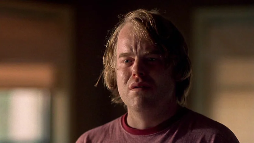 Love Liza (2002) movie still: closeup — A man stands in a dimly lit, out-of-focus indoor space. The subject has visible sweat and tear-filled eyes.