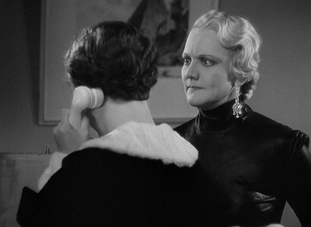 The Thin Man (1934) movie still: medium — An interior space features two women interacting near an indistinct wall hanging. The woman in the…