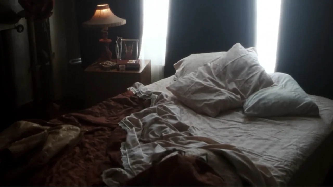 Get Carter (2000) movie still: medium — A dimly lit bedroom features an unmade bed with rumpled white sheets and blankets. A wooden nightstand…