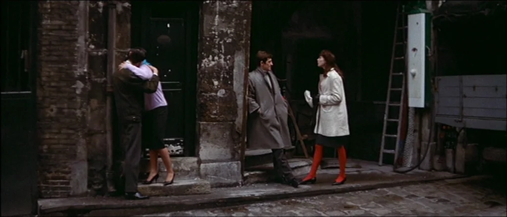 Une Femme Est Une Femme (A Woman Is a Woman) (1961) movie still: wide — A dark urban alleyway features peeling stone walls and a tall metal ladder.…