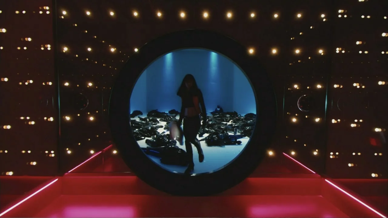 Ultraviolet (2006) movie still: medium — A dark corridor framed by grids of small lit bulbs leads to a glowing circular portal. A woman walks…