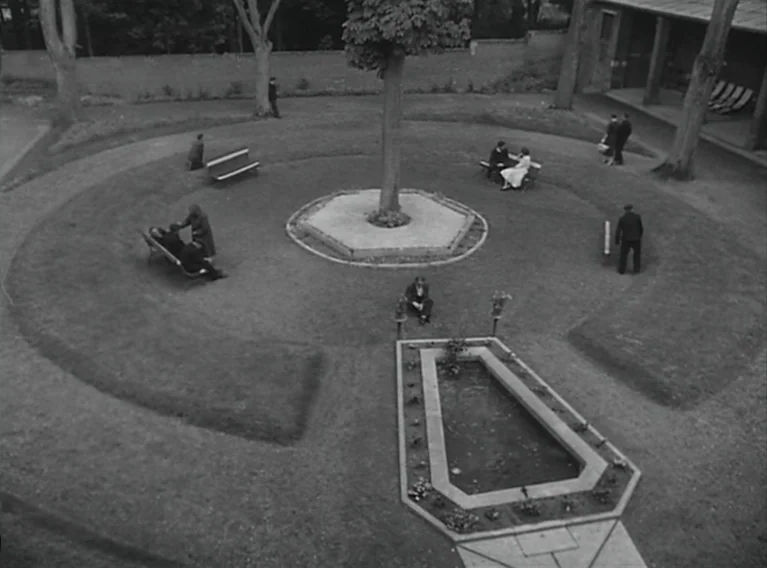 Head Against The Wall (1959) movie still: establishing — A circular park area features a central tree and a geometric reflecting pool. Several…