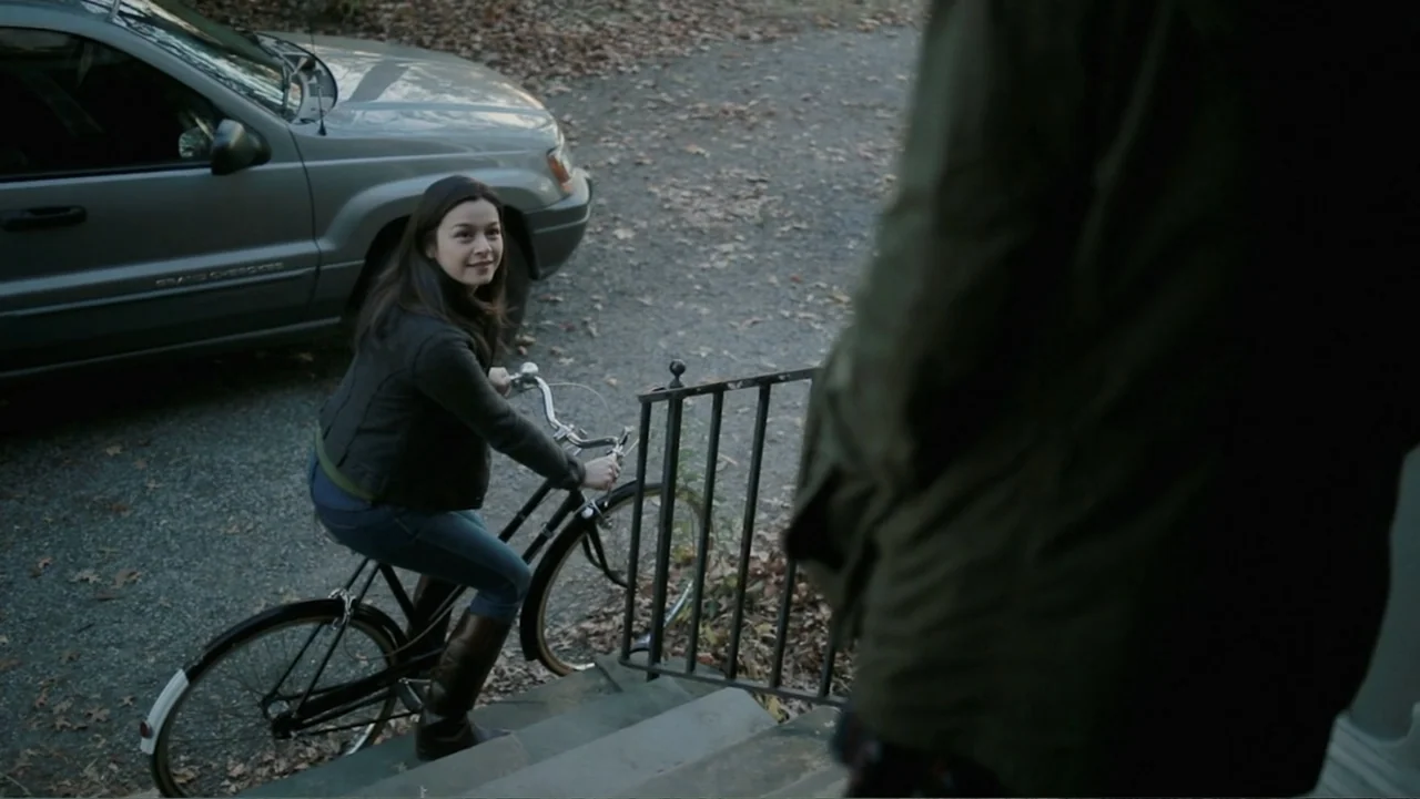 Silent House (2011) movie still: medium — A gravel driveway with autumn leaves scattered on the ground leads toward house steps. A young woman on a…