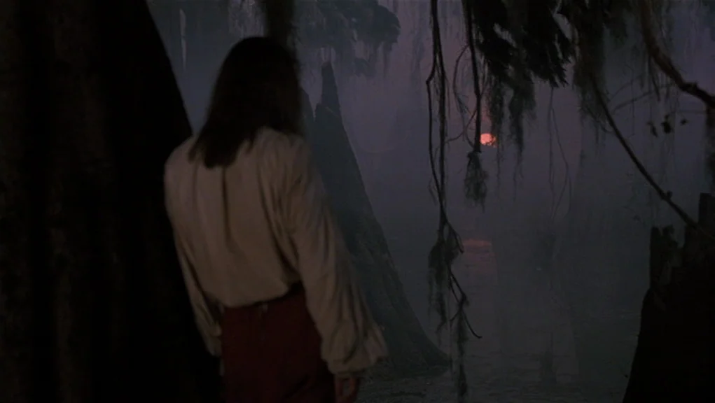 Interview With The Vampire movie still: medium — A dark, fog-covered bayou filled with cypress trees and hanging Spanish moss. A person stands with…