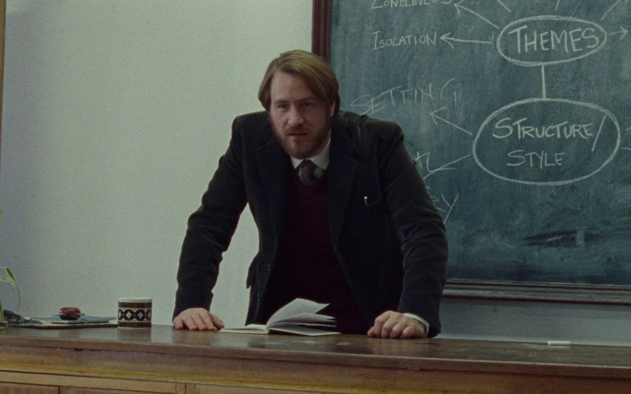 Education (2020) movie still: medium — A classroom features a green chalkboard covered in handwritten educational diagrams and thematic text. A man…