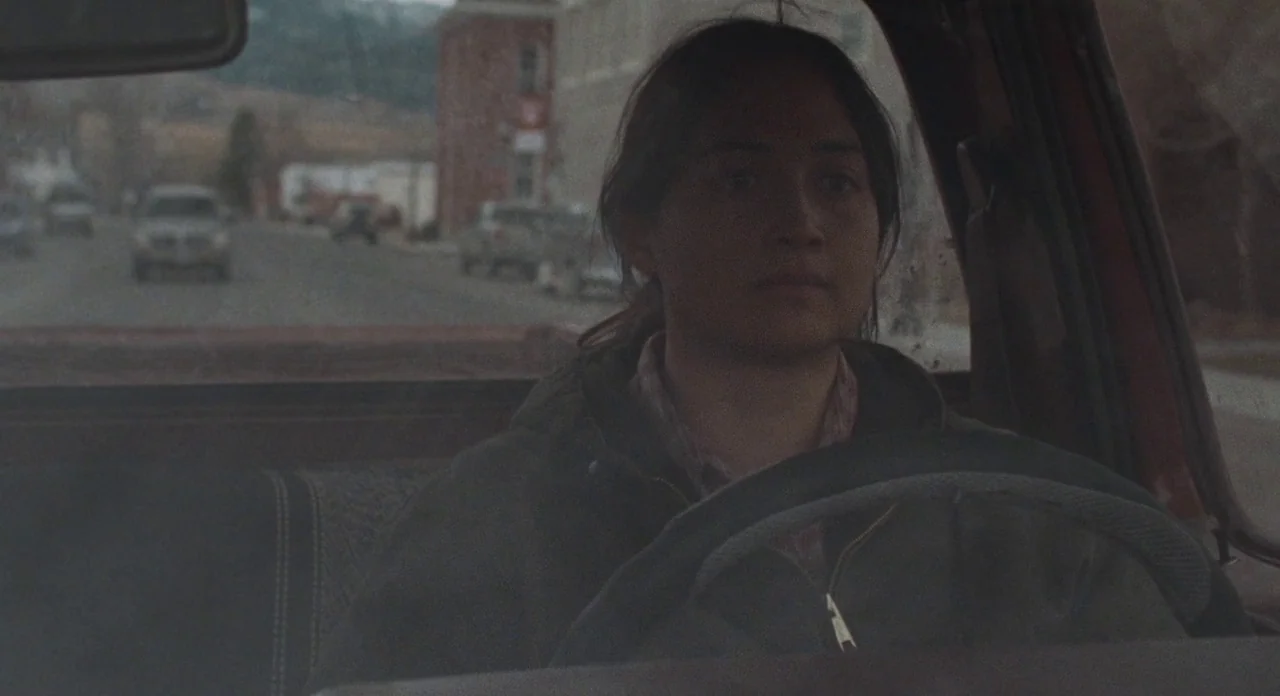 Certain Women (2016) movie still: medium — The interior of a vehicle shows a young woman sitting in the driver seat. Through the windshield, a…