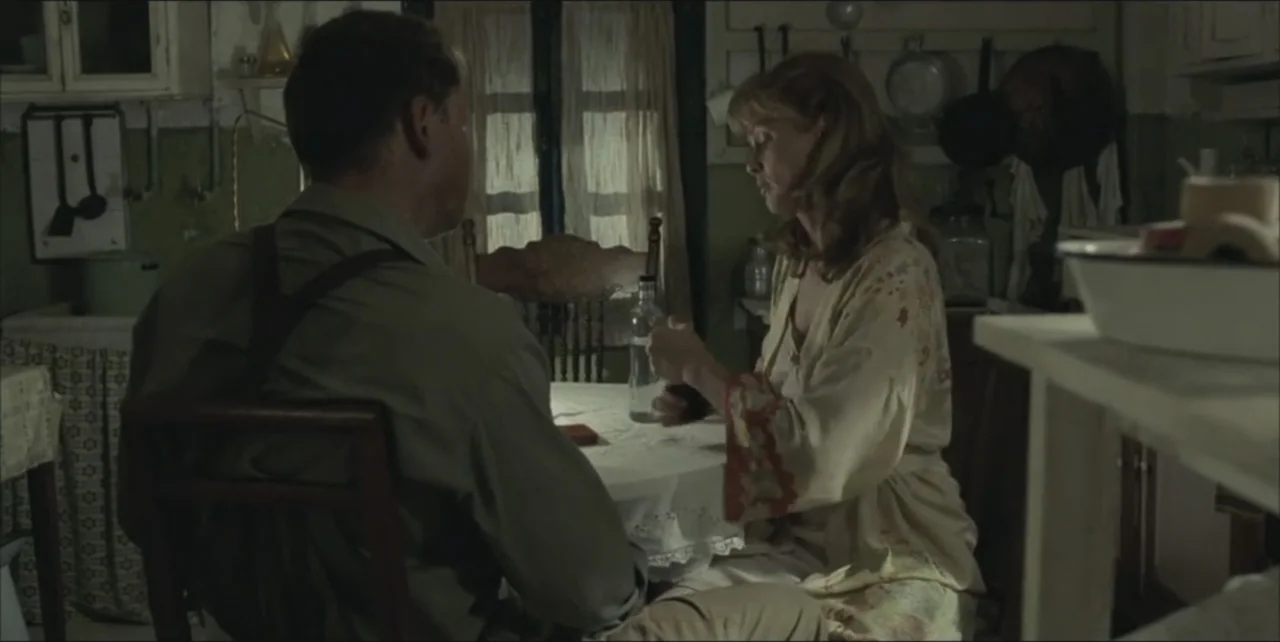 Exorcist: The Beginning (2004) movie still: medium — A rustic dining room features a cluttered table with a white lace cloth. A man in suspenders…
