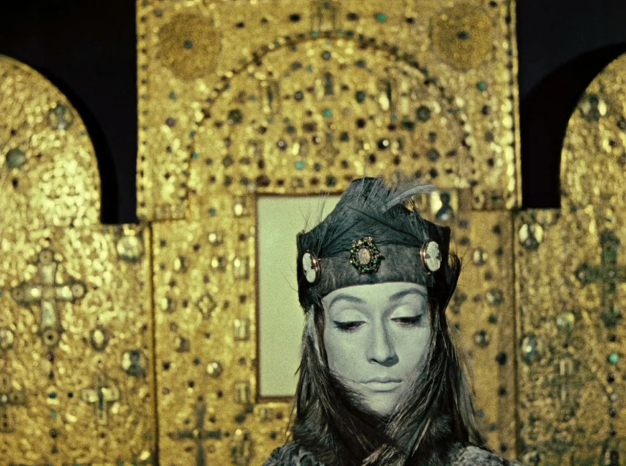 The Colour of Pomegranates (1969) movie still: closeup — A figure stands in front of an ornate, gilded metal wall covered in crosses. The subject…