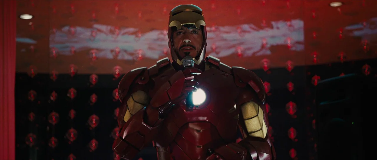 Iron Man 2 (2010) movie still: medium — A dark, dimly lit event space features a decorative background of small red lights. A man wearing an Iron…