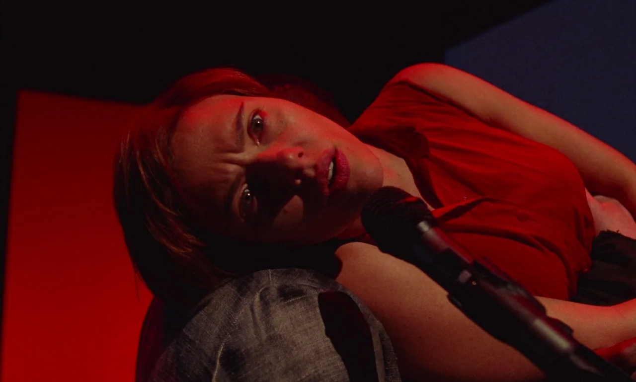 Marriage Story movie still: closeup — A dark space with a vibrant red light casting sharp shadows on the subject. A woman lies on her side, holding…
