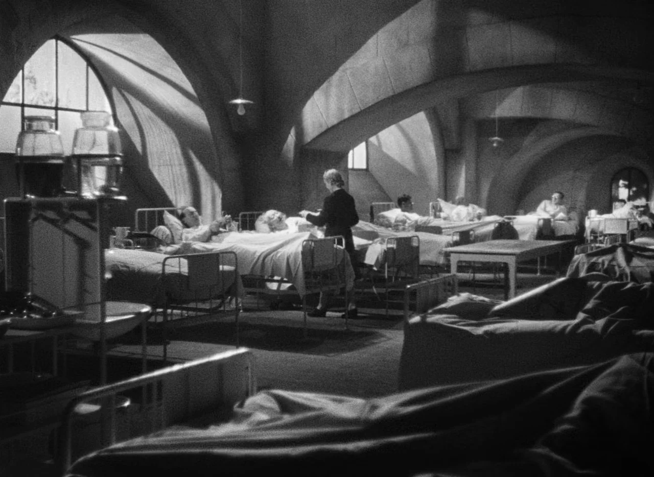 Le Corbeau (1943) movie still: wide — A stone hospital ward features arched ceilings and rows of metal beds.