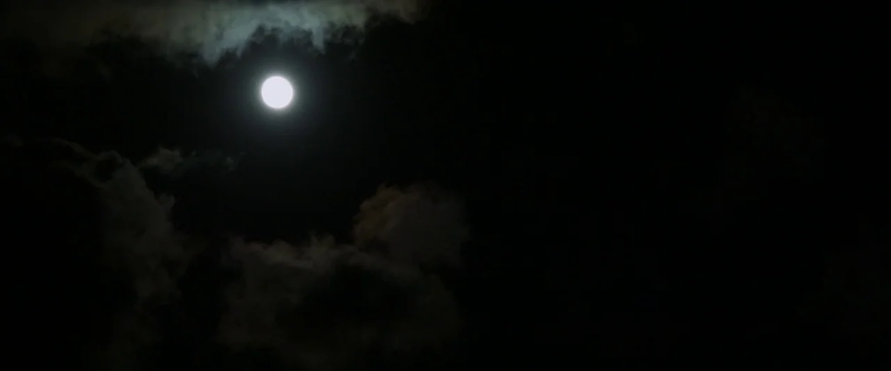 The Monster (2016) movie still: establishing — A bright full moon glows in a dark, cloud-filled night sky. Wispy and dense clouds move across the…