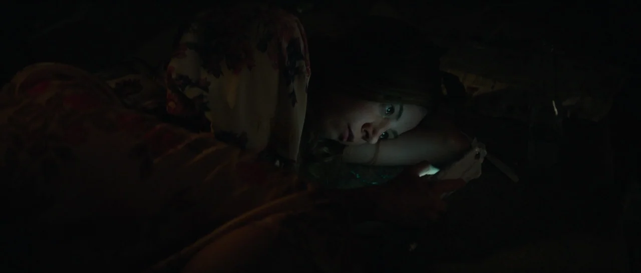 Ingrid Goes West (2017) movie still: closeup — A dimly lit room at night features a person lying on a soft surface. The individual stares at their…