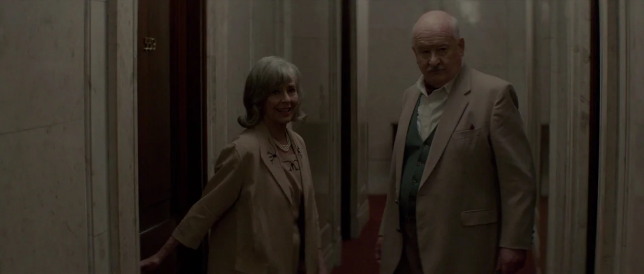 The Two Faces of January (2014) movie still: medium — A dimly lit hotel corridor features marble walls and dark wood door frames. An elderly man and…
