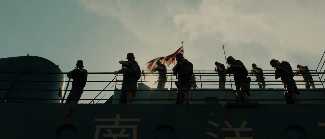 Unbroken (2014) movie still: wide — A line of soldiers stands along the metal railing of a military ship's deck. They hold rifles in firing…
