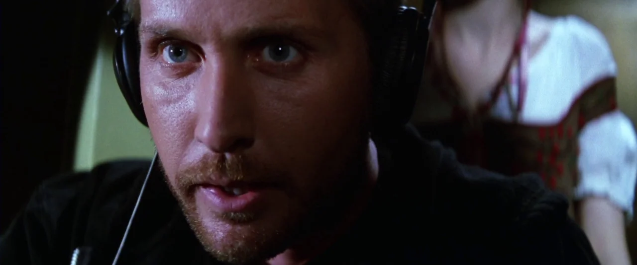 Mission: Impossible (1996) movie still: closeup — A dimly lit room with recording equipment and dark walls. A man wearing black headphones looks…