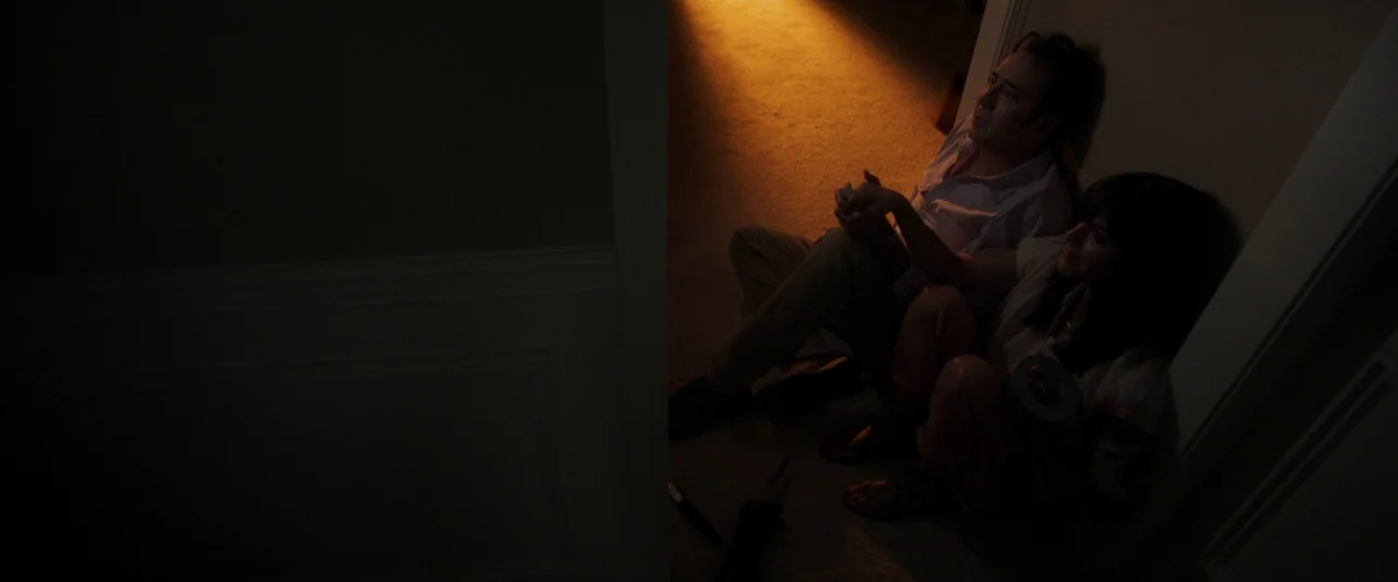 Mom and Dad (2017) movie still: medium — Two individuals sit on the floor of a dark enclosed space illuminated by light. A man and a woman huddle…