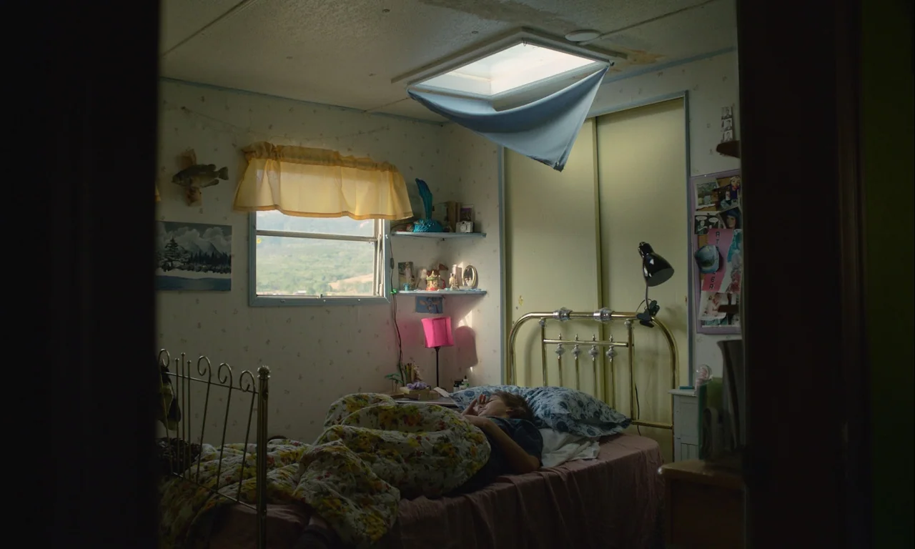 Mickey and the Bear (2019) movie still: wide — A cluttered small bedroom with floral wallpaper and a metal bed frame. A teenager sleeps in the bed…