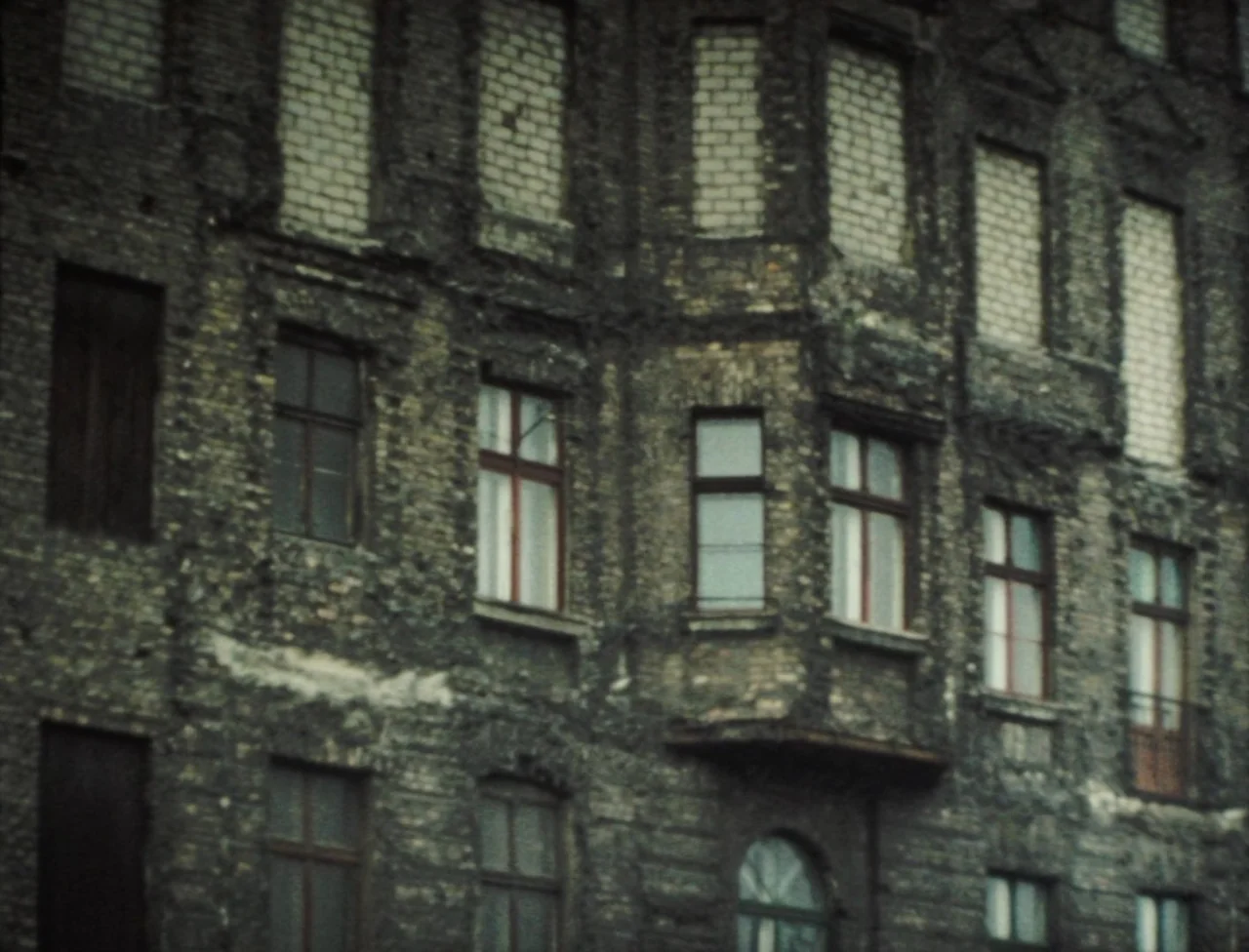 Nekromantik (1988) movie still: establishing — An aging multi-story masonry building features weathered brickwork and partially bricked-up window…