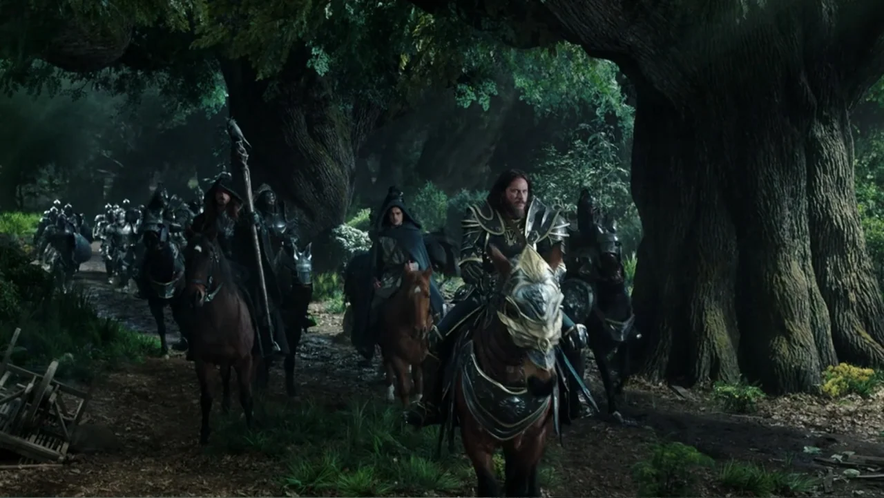 Warcraft (2016) movie still: wide — An ancient woodland clearing features massive thick trees and a dirt trail path. Several armored riders on…