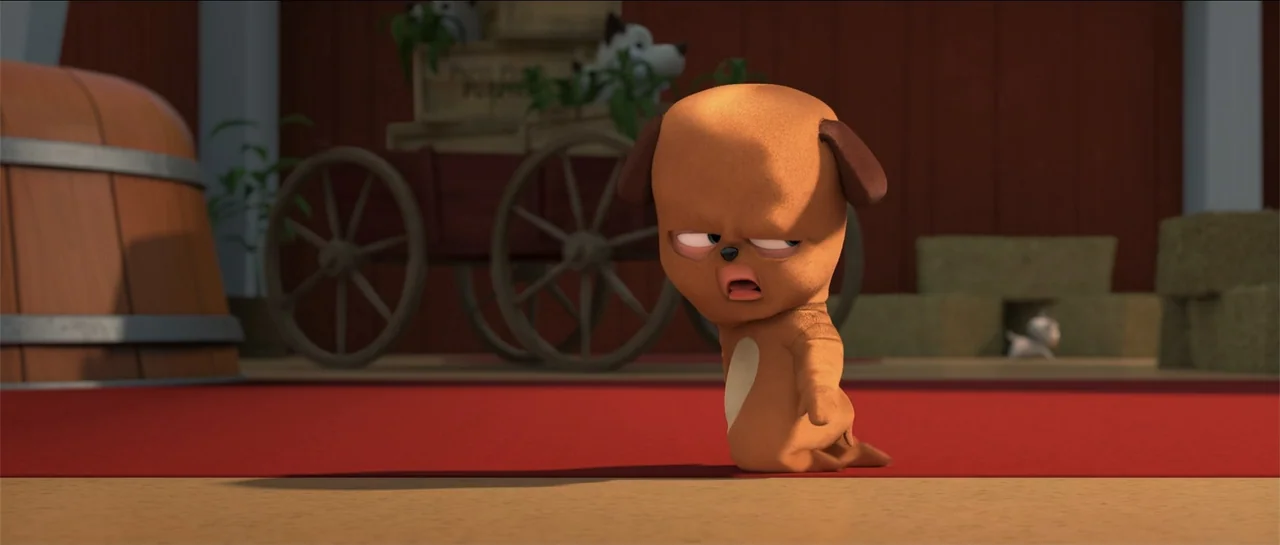 The Boss Baby (2017) movie still: medium — A wooden barn interior contains a red rug and a wooden wagon wheel. A small cartoon-style brown puppy…