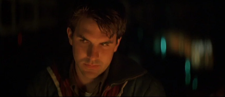 All The Real Girls (2003) movie still: closeup — A dark urban environment at night with blurred colored city lights in the background. A young man…