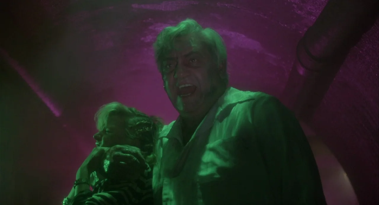 Vamp (1986) movie still: medium — A curved tunnel environment is illuminated by jarring green and magenta artificial neon lights. A man in a white…
