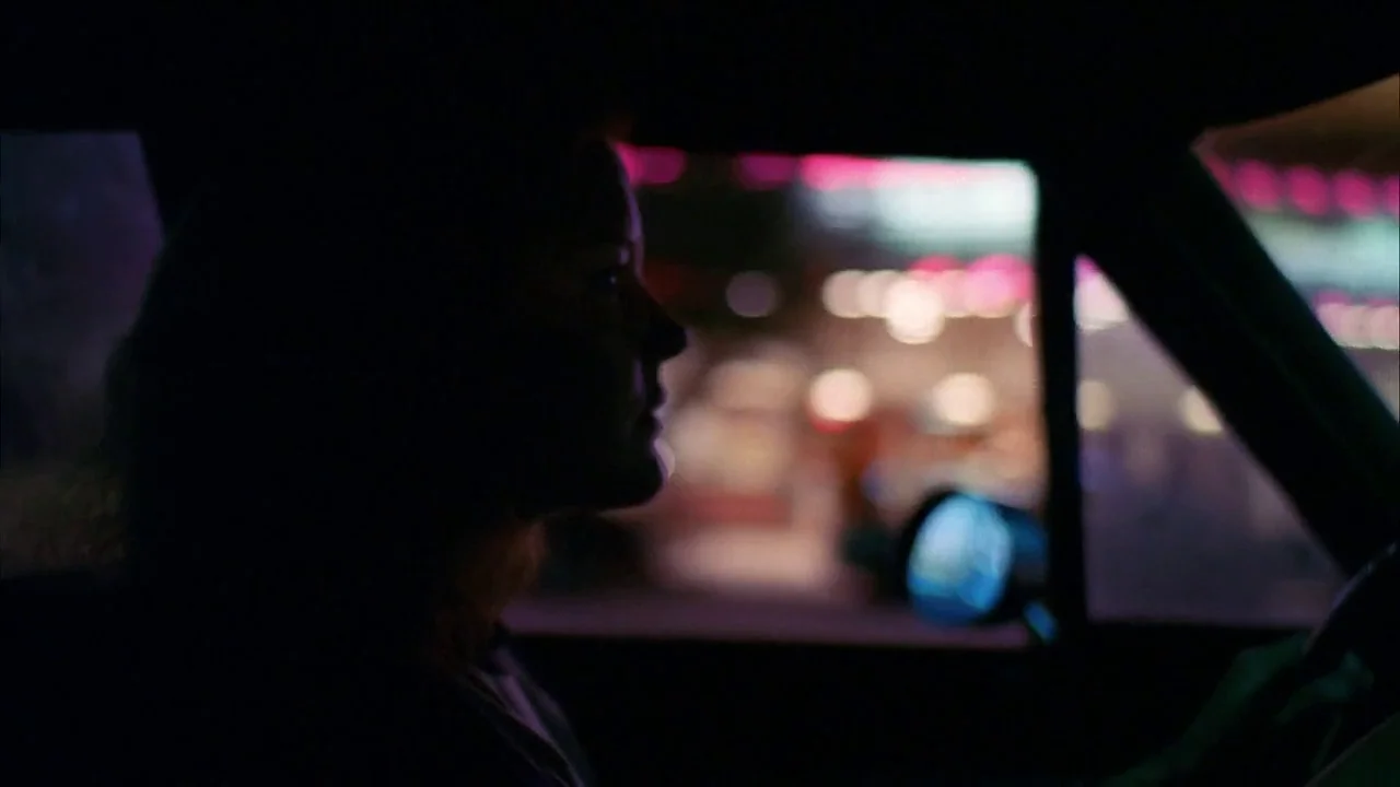 The Slumber Party Massacre (1982) movie still: closeup — A dark car interior at night with a blurred urban environment outside the window. A woman…