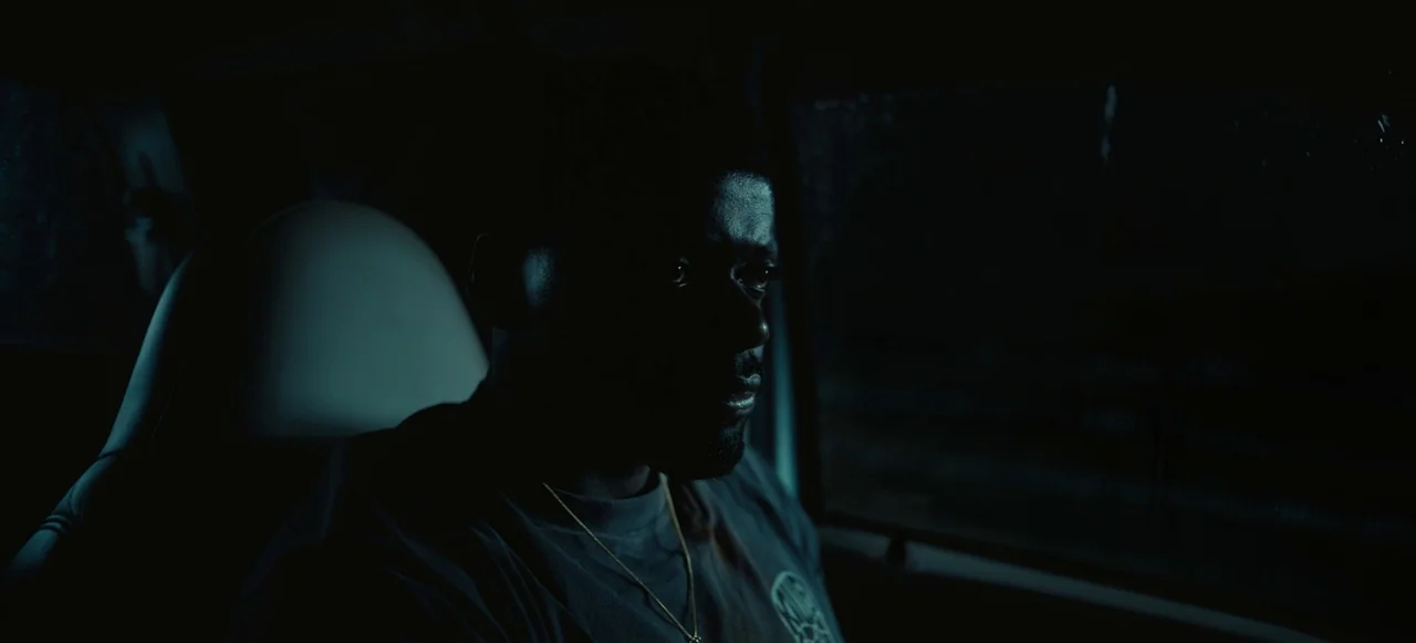 Nope (2022) movie still: medium — The interior of a dark car at night with rain droplets on the window. A man sits in the driver seat looking out…