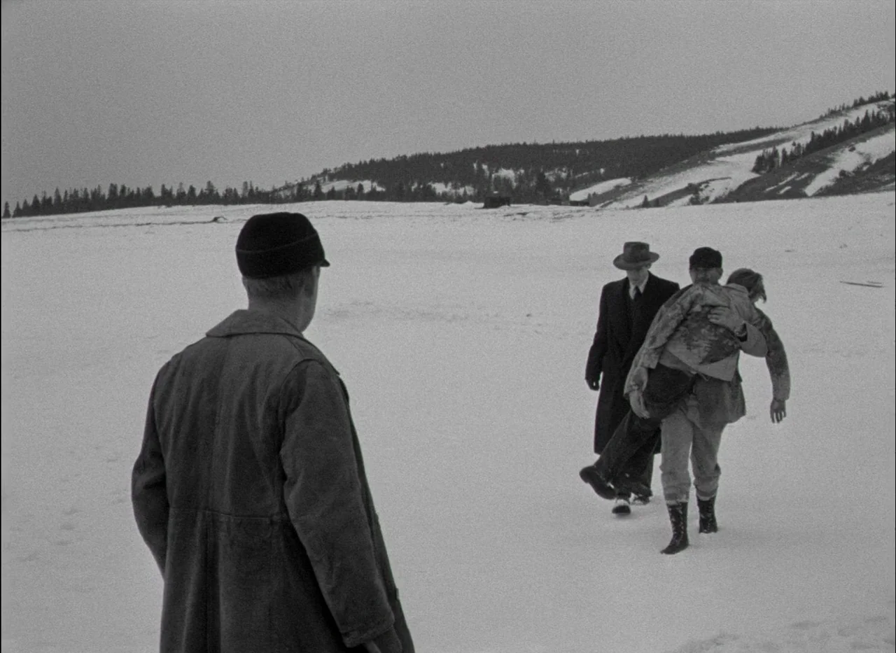 On Dangerous Ground (1951) movie still: wide — An open, snow-covered landscape stretches toward a treeline beneath an overcast gray sky. One man in…