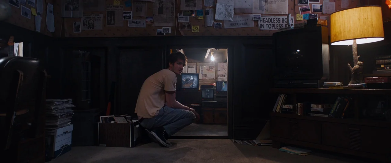 Under The Silver Lake (2018) movie still: wide — A dimly lit room with walls covered in newspaper clippings and investigation notes. A young man…