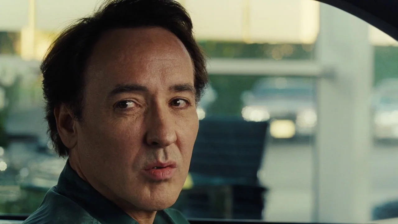 Love & Mercy (2014) movie still: closeup — A man sits inside a vehicle with large windows overlooking a bright exterior parking lot. The man is…