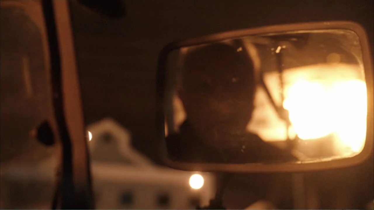 Get Smart (2008) movie still: closeup — A side view mirror of a vehicle reflects a person in darkness. Intense orange light flares from outside…