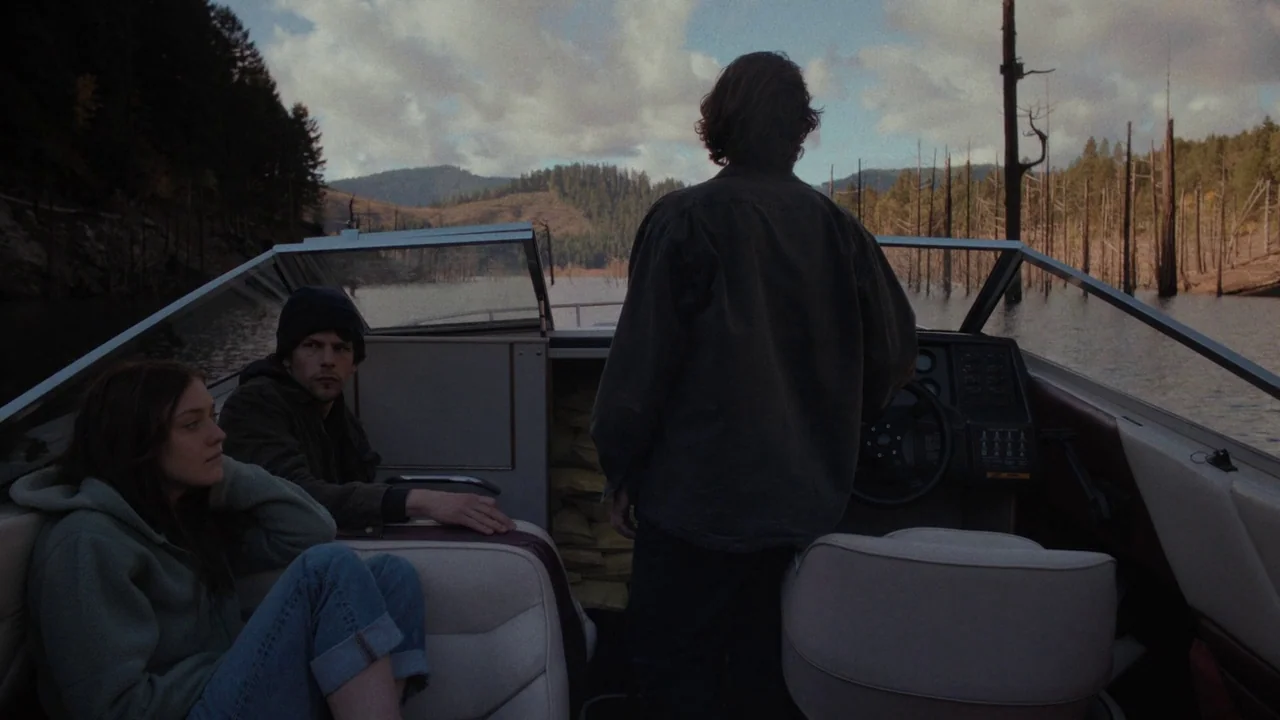 Night Moves (2013) movie still: medium — A motorboat travels through a calm lake surrounded by forested hills and dead trees. Three individuals are…