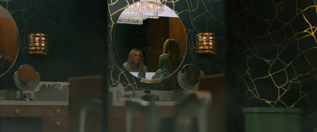 Don’t Worry Darling (2022) movie still: medium — A 1950s style bathroom features teal wallpaper with gold branching cracks. A woman gazes into a…
