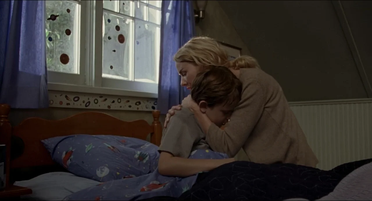 The Ring Two (2005) movie still: medium — A child's bedroom features a wood-frame bed with patterned blue space-themed sheets. A woman kneels on the…