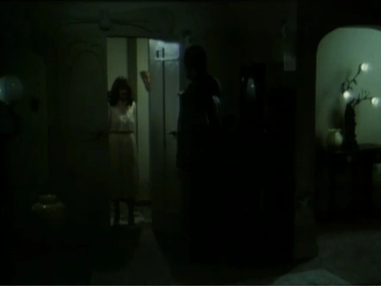 Curtains (1995) movie still: medium — A dimly lit interior space with furniture visible in the foreground and a door frame. A man stands in shadow…