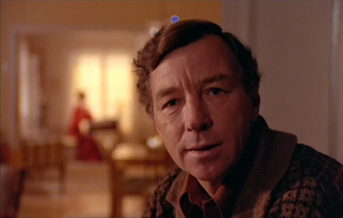 Autumn Sonata (1978) movie still: closeup — A man stands in a domestic setting with soft lighting and neutral color tones. He gazes forward while a…