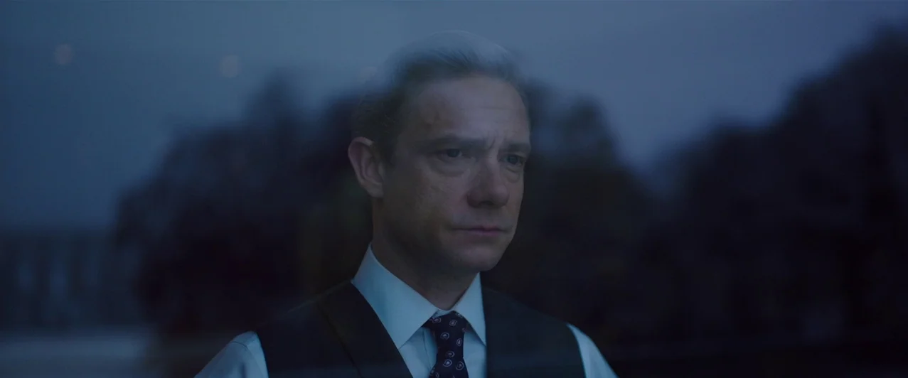 Ghost Stories (2017) movie still: closeup — A man viewed through a reflective glass pane against a dark outdoor evening landscape. He remains still…